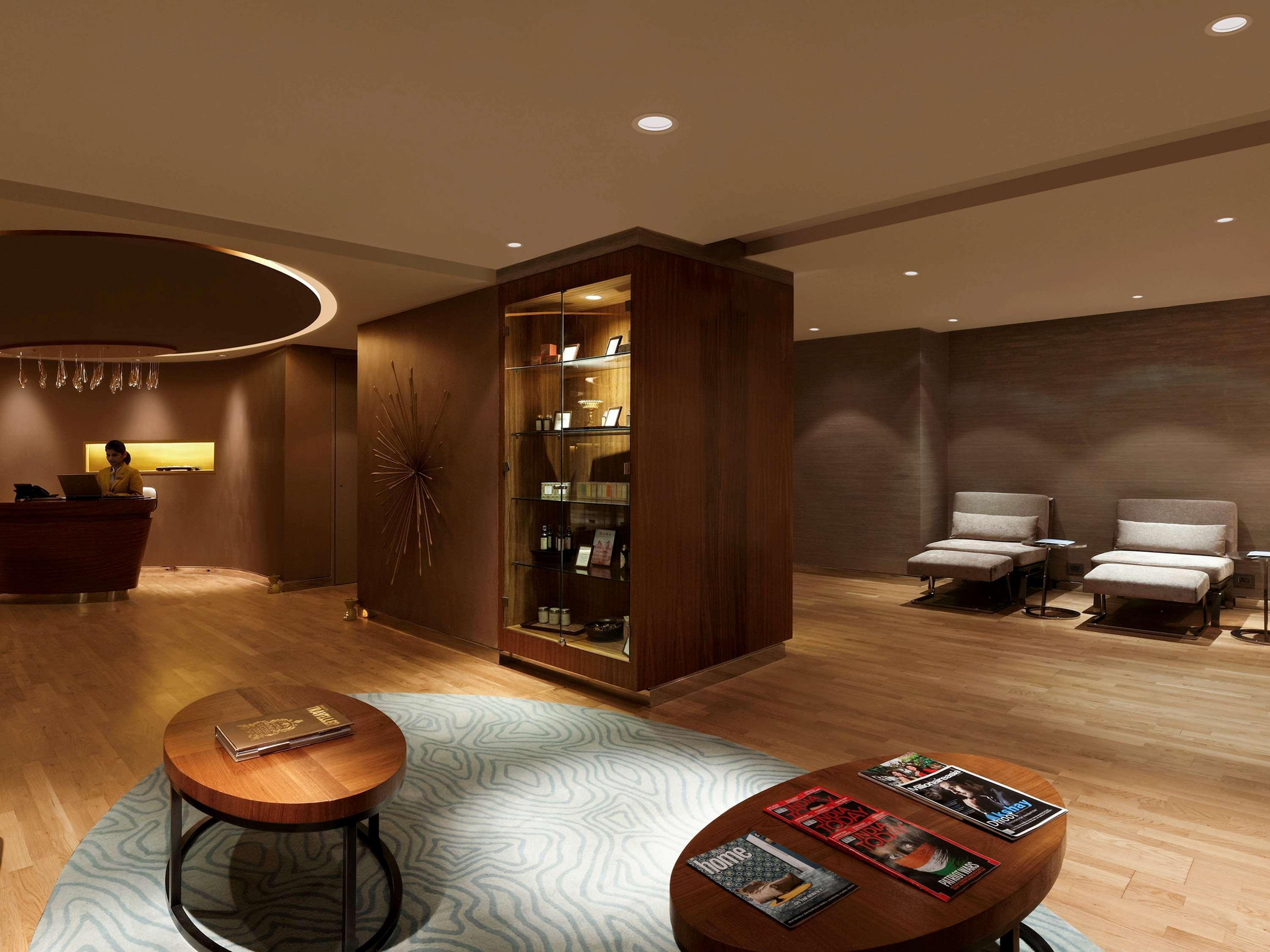 노보텔 뉴델리 인터내셔널 에어포트 언 아코르 호텔 브랜드 외부 사진 The photo shows a modern and elegant interior space, likely a lounge or waiting area. The flooring is wooden, adding warmth to the atmosphere. In the foreground, there are round coffee tables with magazines on them. 

To one side, there's a display c